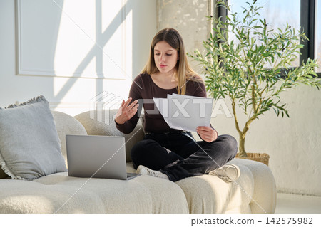 Smiling young woman with business, educational important papers, laptop in home 142575982
