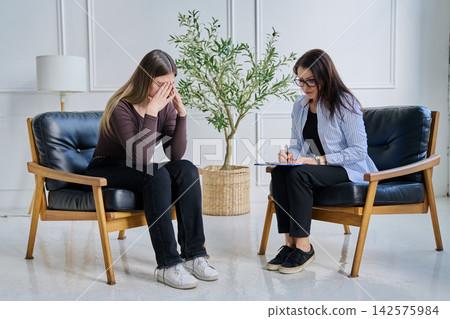 Sad crying young woman patient in therapy session with female psychologist Sad crying young woman patient in therapy session with female psychologist 142575984