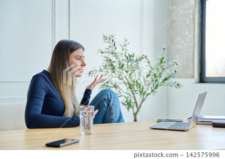 Surprised young woman using laptop for video chat sitting at a table Surprised young woman using laptop for video chat sitting at a table 142575996