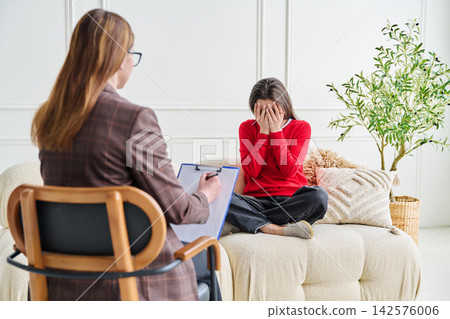 Sad teenage female patient in therapy session in psychologist office. Professional mental support Sad teenage female patient in therapy session in psychologist office. Professional mental support 142576006