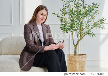 Portrait of young businesswoman sitting on couch in office with smartphone 142576009