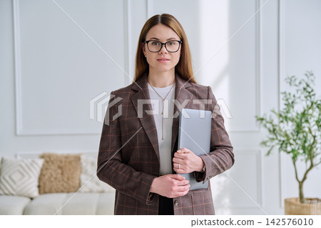 Successful woman entrepreneur or teacher in smart casual attire, holding laptop in office Successful woman entrepreneur or teacher in smart casual attire, holding laptop in office 142576010