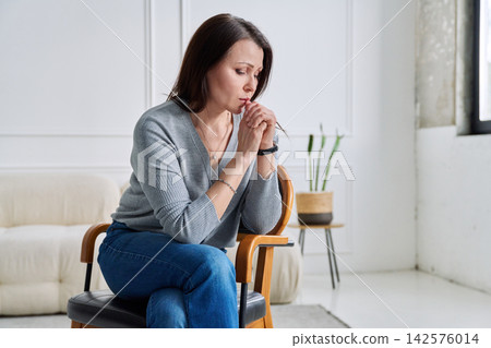 Depressed worried mature woman sitting on a chair, at home Depressed worried mature woman sitting on a chair, at home 142576014