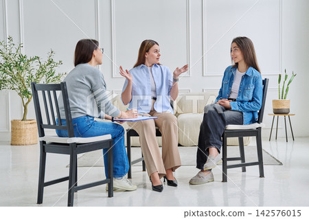 Professional female psychologist or coach conducting a group therapy session with two young women Professional female psychologist or coach conducting a group therapy session with two young women 142576015