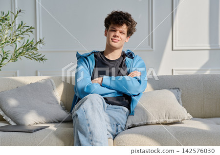 Portrait of handsome young man with curly hair sitting on sofa Portrait of handsome young man with curly hair sitting on sofa 142576030