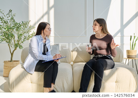 Professional female psychologist, counselor listening to young woman client during therapy session Professional female psychologist, counselor listening to young woman client during therapy session 142576034