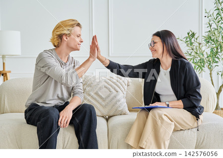 Happy female psychologist giving high five to smiling teenage boy patient Happy female psychologist giving high five to smiling teenage boy patient 142576056