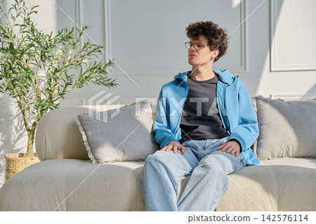 Portrait of handsome young man with curly hair sitting on sofa Portrait of handsome young man with curly hair sitting on sofa 142576114
