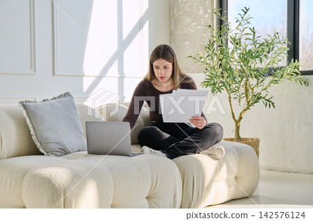 Smiling young woman with business, educational important papers, laptop in home Smiling young woman with business, educational important papers, laptop in home 142576124