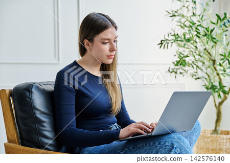 Portrait of young woman sitting on chair with laptop 142576140