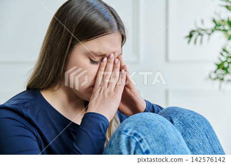 Unhappy upset young woman sitting on chair at home Unhappy upset young woman sitting on chair at home 142576142