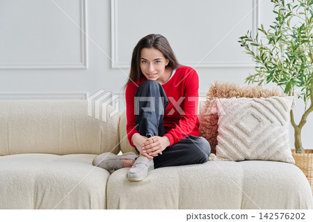 Portrait of beautiful young teenage girl sitting on sofa looking at camera Portrait of beautiful young teenage girl sitting on sofa looking at camera 142576202