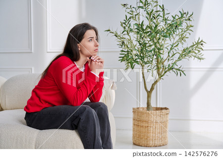 Sad unhappy stressed young woman sitting at home on sofa Sad unhappy stressed young woman sitting at home on sofa 142576276