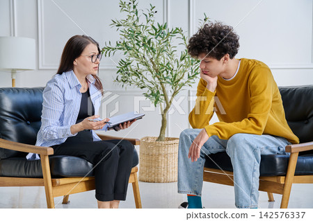 Young male patient in therapy session talking with female psychotherapist Young male patient in therapy session talking with female psychotherapist 142576337