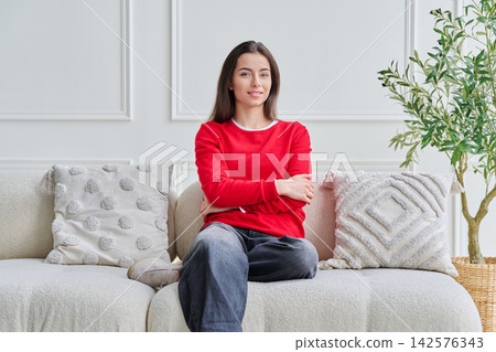 Portrait of beautiful young teenage girl sitting on sofa looking at camera Portrait of beautiful young teenage girl sitting on sofa looking at camera 142576343