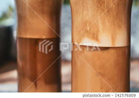 Close-up of two tall glasses filled with iced frothy coffee beverages Close-up of two tall glasses filled with iced frothy coffee beverages 142576809
