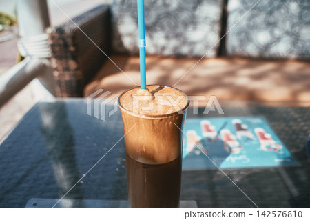 Close up view of a cold iced coffee drink in a tall glass with blue straw Close up view of a cold iced coffee drink in a tall glass with blue straw 142576810
