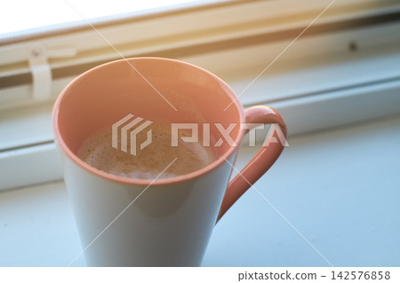 Close-up of a ceramic mug filled with fresh hot coffee placed near a bright window. Close-up of a ceramic mug filled with fresh hot coffee placed near a bright window. 142576858