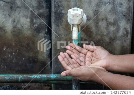 Cupped hands waiting for drop under dirty plastic water tap against concrete wall. Powerful visual for water crisis, climate change, and hygiene issues. Cupped hands waiting for drop under dirty plastic water tap against concrete wall. Powerful visual for water crisis, climate change, and hygiene issues. 142577634