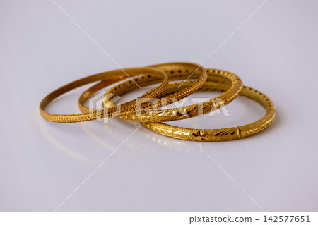 Traditional gold bangles with intricate carved designs placed on white background. Elegant golden jewelry set crafted for bridal wear and wedding ornament. Traditional gold bangles with intricate carved designs placed on white background. Elegant golden jewelry set crafted for bridal wear and wedding ornament. 142577651