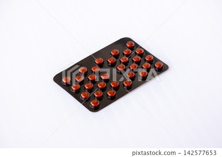 Round pills sealed inside dark blister pack placed on clean white background. Pharmaceutical tablet strip prepared for medical healthcare treatment. Round pills sealed inside dark blister pack placed on clean white background. Pharmaceutical tablet strip prepared for medical healthcare treatment. 142577653