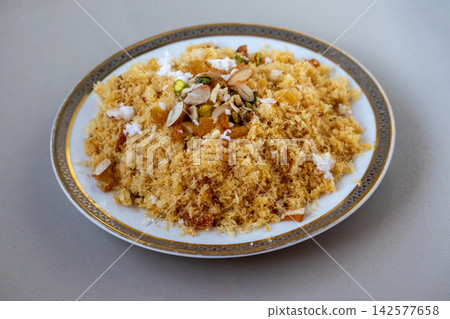 Fried crispy laccha semai dessert garnished with nuts raisins and grated coconut on ceramic plate. Traditional South Asian sweet dish prepared for Eid festival. Fried crispy laccha semai dessert garnished with nuts raisins and grated coconut on ceramic plate. Traditional South Asian sweet dish prepared for Eid festival. 142577658