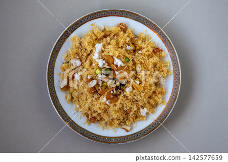 Sweet crispy fried laccha semai vermicelli dessert topped with nuts raisins and coconut on plate. Traditional Bengali sweet dish prepared for festive celebration. Top view. Sweet crispy fried laccha semai vermicelli dessert topped with nuts raisins and coconut on plate. Traditional Bengali sweet dish prepared for festive celebration. Top view. 142577659