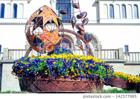 Large forged Easter egg and flower bed with pansies near church in Lviv, Ukraine 142577995
