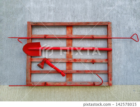 Red fire safety shield with essential fire fighting tools on wall Red fire safety shield with essential fire fighting tools on wall 142578015