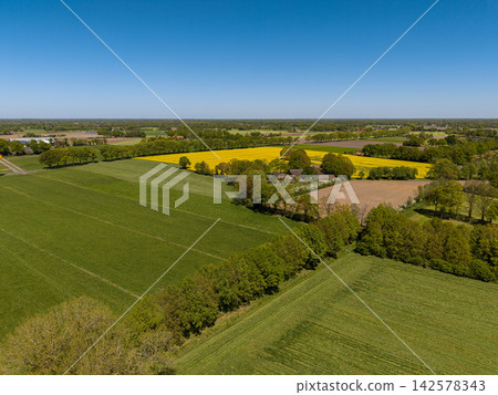 High angle wide horizontal aerial drone photograph of farmstead, yellow rapeseed field, pastures, and tree lines in rural Gelderland, Achterhoek, Netherlands on sunny spring day High angle wide horizontal aerial drone photograph of farmstead, yellow rapeseed field, pastures, and tree lines in rural Gelderland, Achterhoek, Netherlands on sunny spring day 142578343