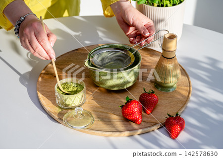 Authentic Moment of Stirring Matcha with Strawberries. Authentic candid moment of stirring matcha in ceramic bowl alongside strawberries on kitchen cutting board. Motion and warmth of whisking with ba 142578630