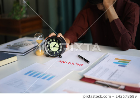 Businessman working on office desk, holding clock with deadline document and running hourglass on the table. Time management concept. 142578689