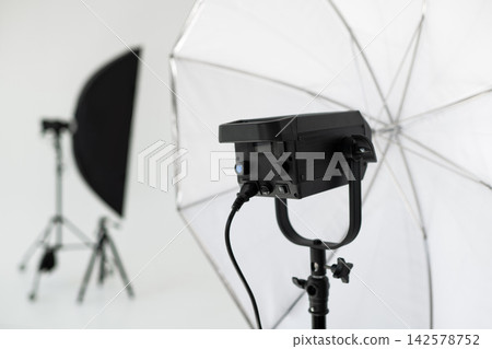 Professional studio flash lighting setup with white translucent umbrella reflector in bright photo room 142578752
