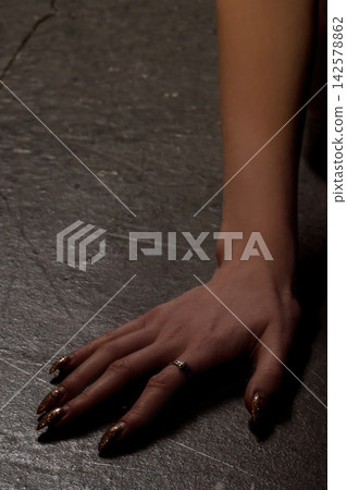 Hand resting on a dark surface, showing off nail polish and a ring in a dimly lit setting Hand resting on a dark surface, showing off nail polish and a ring in a dimly lit setting 142578862