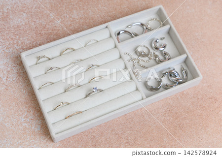 Jewelry organizer holds rings and earrings on beige surface for easy access and storage at home Jewelry organizer holds rings and earrings on beige surface for easy access and storage at home 142578924
