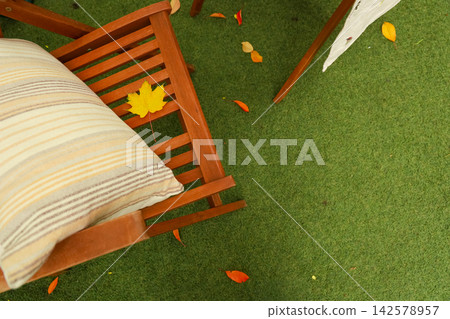 Colorful leaves surround a wooden chair with a striped cushion on a grassy surface during a quiet afternoon in a cozy outdoor space Colorful leaves surround a wooden chair with a striped cushion on a grassy surface during a quiet afternoon in a cozy outdoor space 142578957