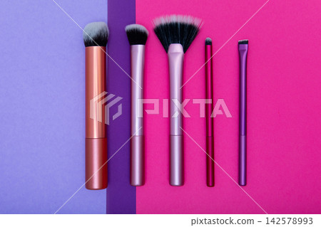 Different types of makeup brushes arranged on a purple and pink background showing various sizes and shapes used for applying cosmetics Different types of makeup brushes arranged on a purple and pink background showing various sizes and shapes used for applying cosmetics 142578993