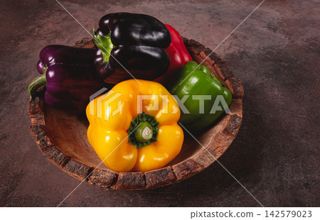 A collection of colorful bell peppers, in a wooden bowl, on a dark surface, top view, no people A collection of colorful bell peppers, in a wooden bowl, on a dark surface, top view, no people 142579023