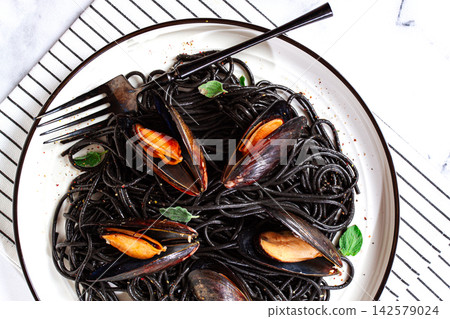 Black spaghetti with mussels, on a white plate with a fork, on a striped napkin,marble background, homemade, no people Black spaghetti with mussels, on a white plate with a fork, on a striped napkin,marble background, homemade, no people 142579024