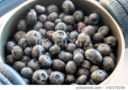 Ripe Blueberries in a Bowl Beside Headphones. Fresh ripe blueberries fill a bowl beside headphones, a conceptual close up blending summer fruit and audio technology, a creative and minimal idea  142579280