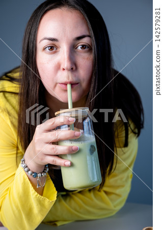 Woman Drinking Matcha Latte Close-up, Summer Refreshment. Close-up of woman sipping vibrant matcha latte through straw in bright summer setting. Detail of lips and glass jar with green frothy drink. Woman Drinking Matcha Latte Close-up, Summer Refreshment. Close-up of woman sipping vibrant matcha latte through straw in bright summer setting. Detail of lips and glass jar with green frothy drink. 142579281