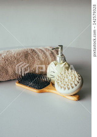 Rolled towel with bamboo brush and soap dispenser on table. Rolled beige towel with bamboo hair brush and ceramic cat soap dispenser on white table, spa accessories and natural materials self care sti Rolled towel with bamboo brush and soap dispenser on table. Rolled beige towel with bamboo hair brush and ceramic cat soap dispenser on white table, spa accessories and natural materials self care sti 142579328