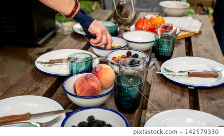 Rustic Outdoor Table with Olives Tomatoes and Peaches. Rustic wooden picnic table set with white enamel plates and bowls of green olives, mixed berries, fresh tomatoes and peaches, with a vintage lant Rustic Outdoor Table with Olives Tomatoes and Peaches. Rustic wooden picnic table set with white enamel plates and bowls of green olives, mixed berries, fresh tomatoes and peaches, with a vintage lant 142579330