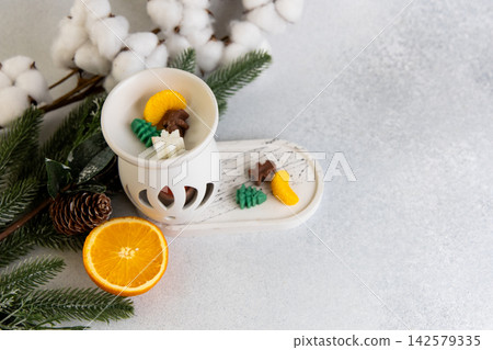 Aroma lamp sits with Christmas wax melts beside fresh orange and pine on a light surface Aroma lamp sits with Christmas wax melts beside fresh orange and pine on a light surface 142579335