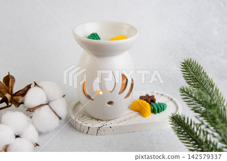 Aroma lamp with Christmas wax melts sits on a table with cotton and pine branches nearby Aroma lamp with Christmas wax melts sits on a table with cotton and pine branches nearby 142579337
