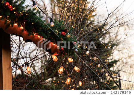Decorative lights and greenery adorn a winter Christmas scene in a festive outdoor area during the day Decorative lights and greenery adorn a winter Christmas scene in a festive outdoor area during the day 142579349