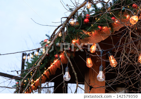 String lights Christmas decorate an outdoor space with greenery and ornaments during the evening hours String lights Christmas decorate an outdoor space with greenery and ornaments during the evening hours 142579350
