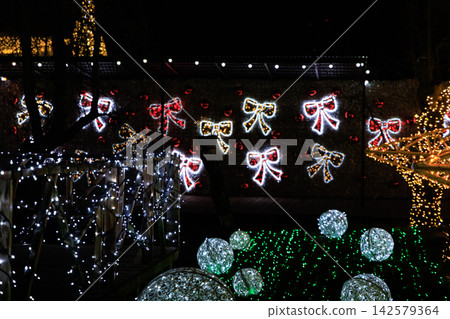 Colorful Christmas lights shine at night with decorations shaped like bows and bright spheres on display Colorful Christmas lights shine at night with decorations shaped like bows and bright spheres on display 142579364