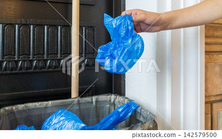 Hand Dropping Used Blue Shoe Cover into Waste Bin. Medical Plastic Waste Concept Hand Dropping Used Blue Shoe Cover into Waste Bin. Medical Plastic Waste Concept 142579500
