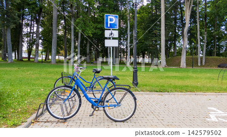 Blue Bicycles Parked in Metal Rack under Parking Sign in Park. Urban Eco Transport Concept Blue Bicycles Parked in Metal Rack under Parking Sign in Park. Urban Eco Transport Concept 142579502